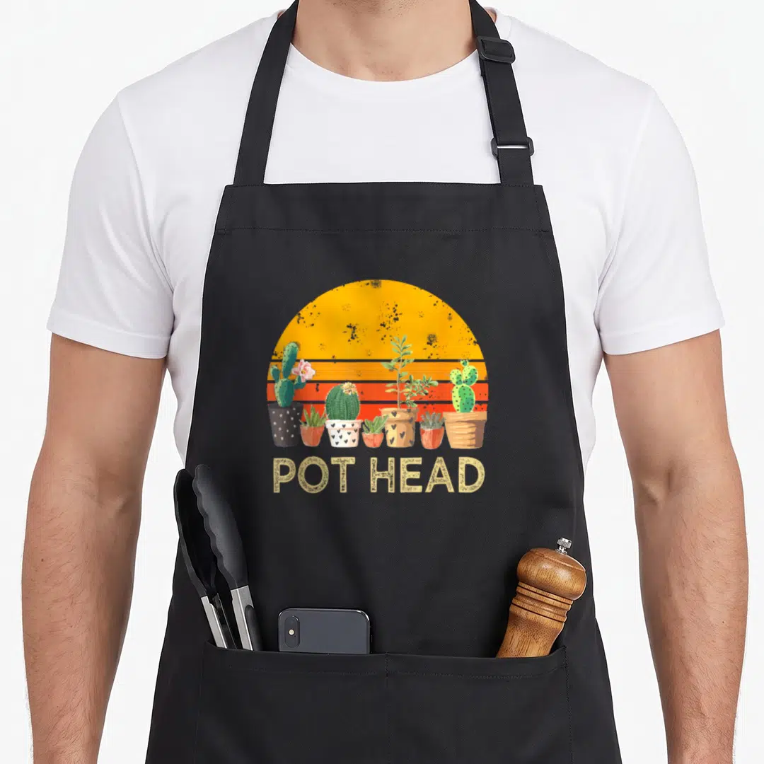 Pot stone apron - Retro sunset with six potted plants and text POT HEAD in yellow — shown on a black cotton canvas apron against a white background