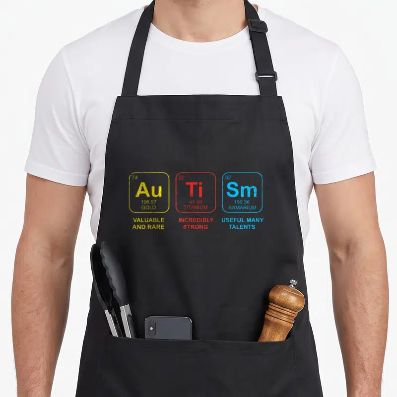 Autism table apron - Three colored periodic table squares showing Au Ti Sm with text Valuable Strong Useful Talents — shown on a black cotton canvas apron against a white background
