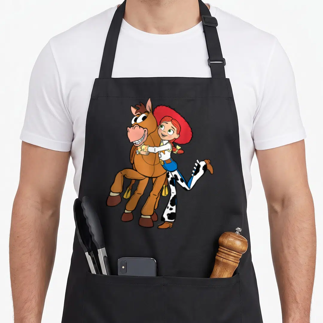 Jessie sheriff apron - Cartoon Jessie hugging Bullseye from the side with leg kicked back in brown red white and blue — shown on a black cotton canvas apron against a white background