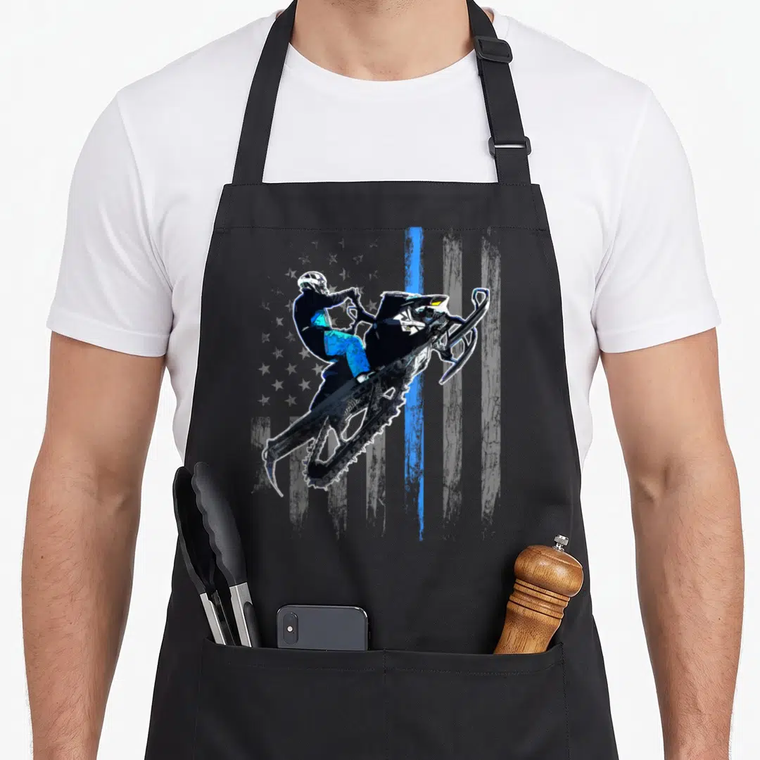 Snowmobile american flag apron - Minimalist snowmobile rider jumping diagonally with vertical blue brushstroke in black — shown on a black cotton canvas apron against a white background