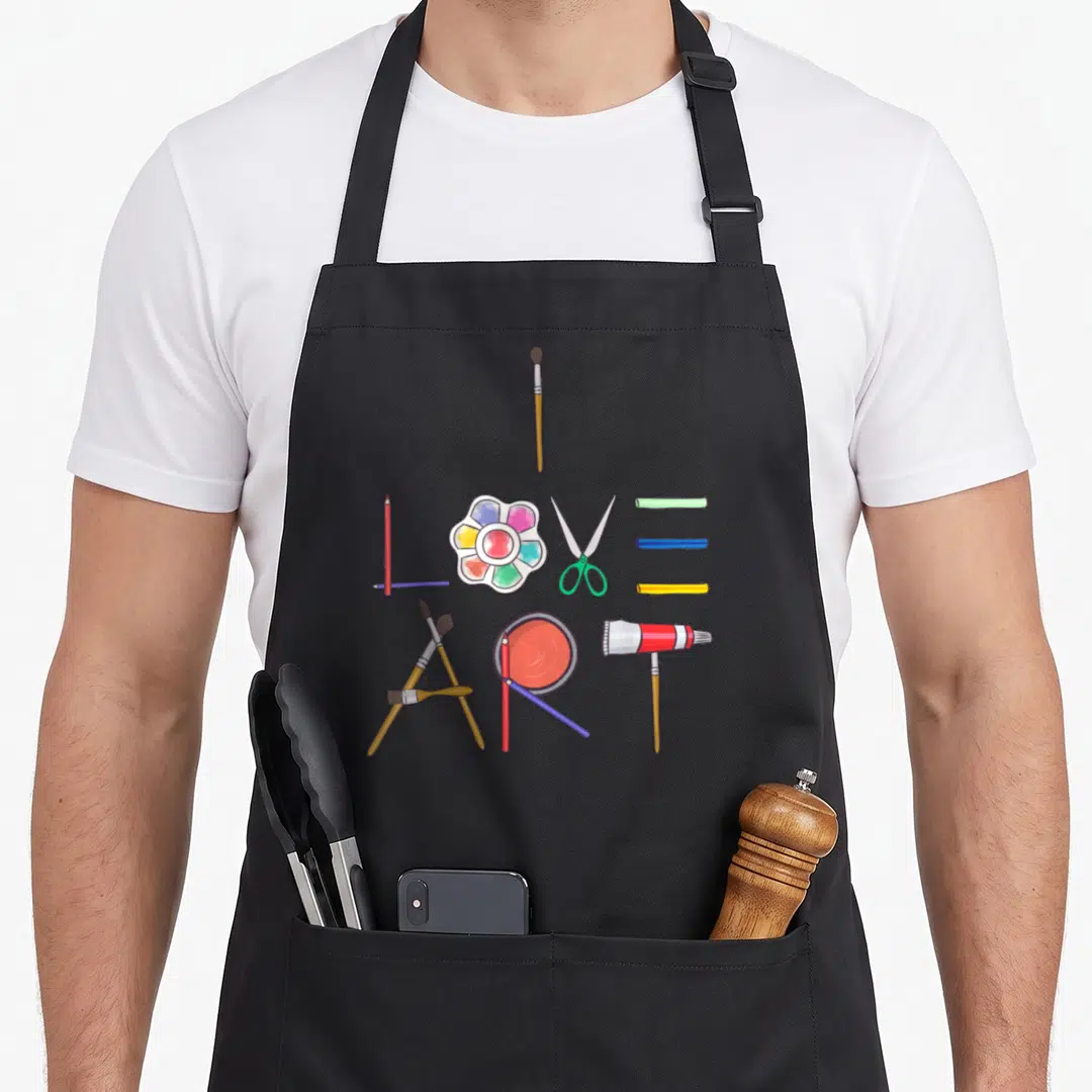 Painting painter apron - Art supplies including brushes pencils scissors and palette spelling I Love Art in cartoon — shown on a black cotton canvas apron against a white background