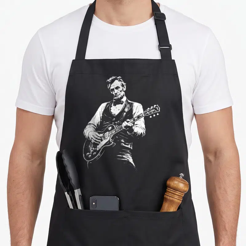 Funny abe playing guitar apron - White line-art illustration of Abraham Lincoln playing an electric guitar — shown on a black cotton canvas apron against a white background