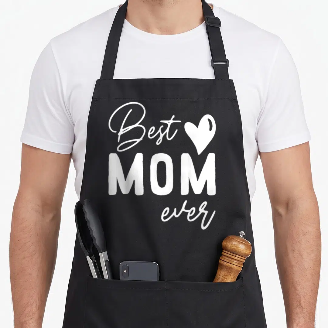 Funny mother daughter apron - White stacked text reading Best MOM ever with a heart shape on black fabric — shown on a black cotton canvas apron against a white background