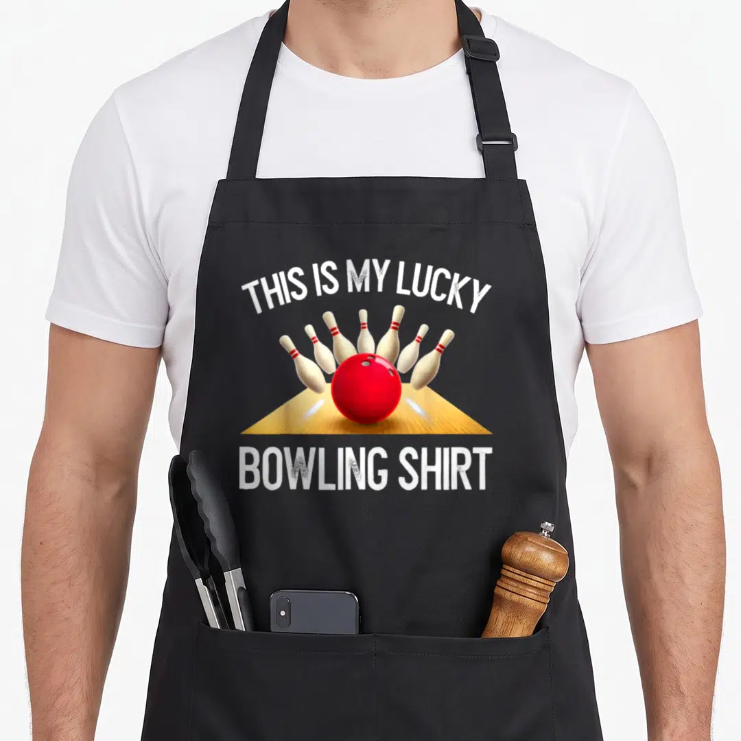 Lucky retro bowling apron - Red bowling ball hitting pins with THIS IS MY LUCKY BOWLING SHIRT text — shown on a black cotton canvas apron against a white background