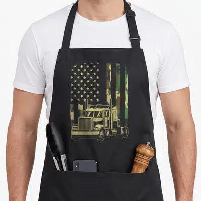 Trucker camouflage american flag apron - Tan semi-truck over stars and camo stripes with distressed finish — shown on a black cotton canvas apron against a white background
