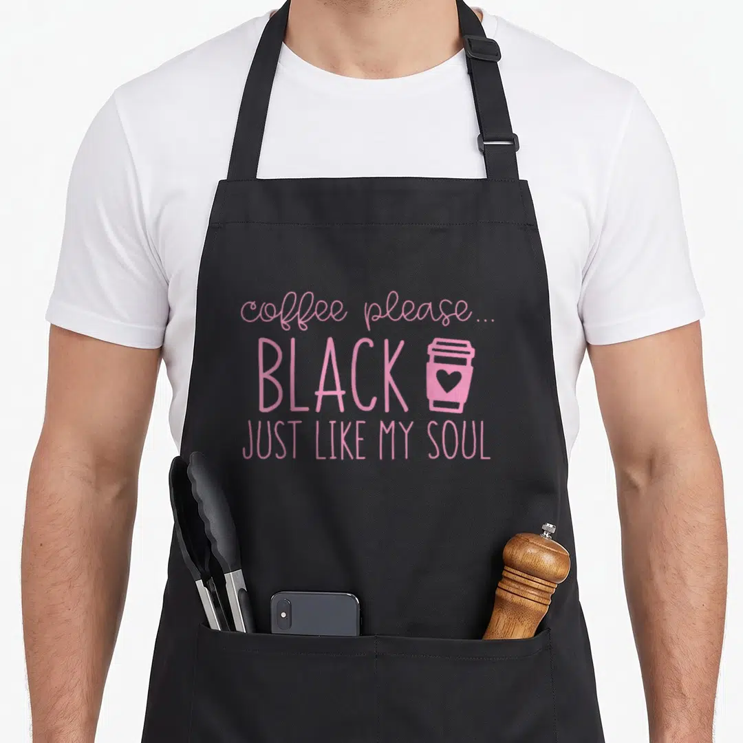 Mug coffee aprons - Pink text reading coffee please just like my soul next to a cup with a heart — shown on a black cotton canvas apron against a white background