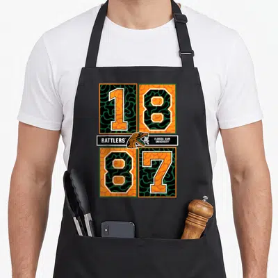 Rattler florida apron - Snake head and 1887 numbers in orange green black white blocks — shown on a black cotton canvas apron against a white background