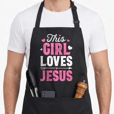 Religious christian aprons - Stacked pink and white text reading This Girl Loves Jesus with hearts and arrow graphic — shown on a black cotton canvas apron against a white background