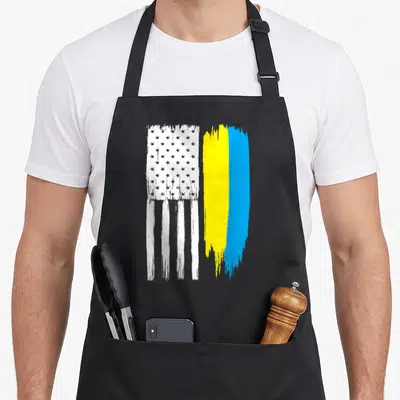 Ukraine ukrainian aprons for women - Two vertical distressed flags with white stars and blue yellow brush strokes — shown on a black cotton canvas apron against a white background