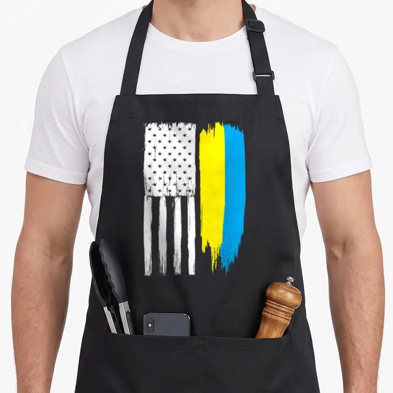 Ukraine ukrainian aprons for women - Two vertical distressed flags with white stars and blue yellow brush strokes — shown on a black cotton canvas apron against a white background