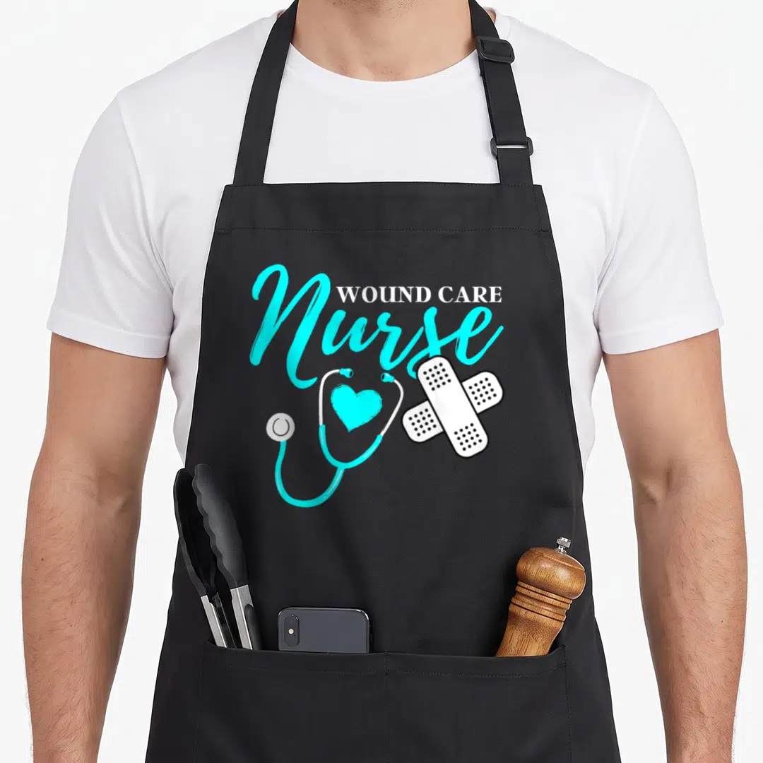 Wound nurses apron - WOUND CARE Nurse text with cyan stethoscope heart and two white crossed bandages — shown on a black cotton canvas apron against a white background