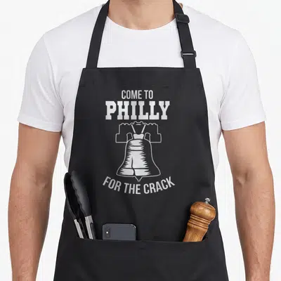 Come phillies apron - White Liberty Bell outline with text COME TO PHILLY FOR THE CRACK on black background — shown on a black cotton canvas apron against a white background