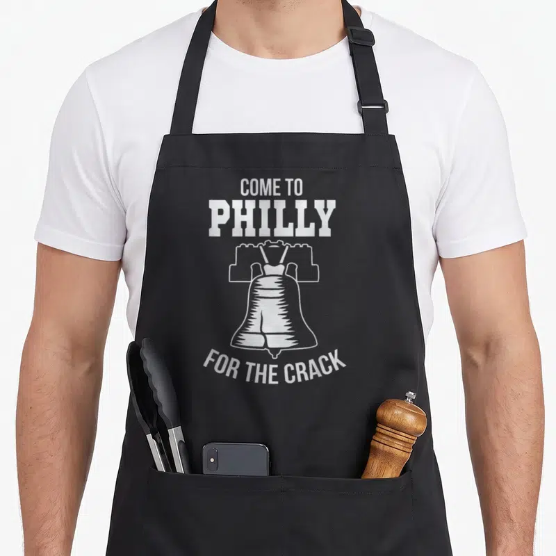 Come phillies apron - White Liberty Bell outline with text COME TO PHILLY FOR THE CRACK on black background — shown on a black cotton canvas apron against a white background