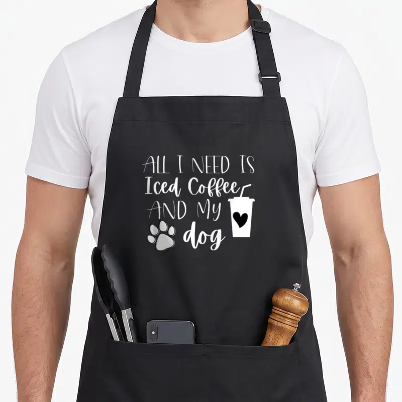 Iced coffee dog apron - Stacked white text reading All I Need Is Iced Coffee And My Dog next to a cup with a black — shown on a black cotton canvas apron against a white background