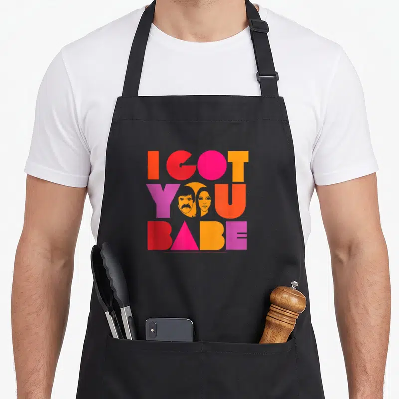 Sonny crew neck apron - Stacked I GOT YOU BABE text in red pink orange purple with two faces inside the O and U of YOU — shown on a black cotton canvas apron against a white background