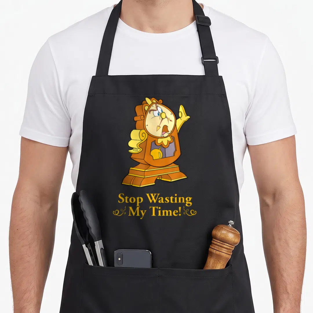 Cogsworth novelty apron - Anthropomorphic brown clock with monocle and yellow text reading Stop Wasting My Time — shown on a black cotton canvas apron against a white background