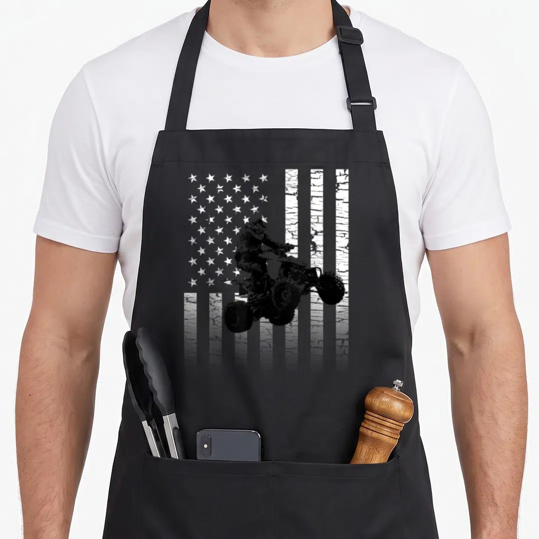 Atv american flag apron - Distressed black and white ATV rider jumping in front of US flag silhouette — shown on a black cotton canvas apron against a white background