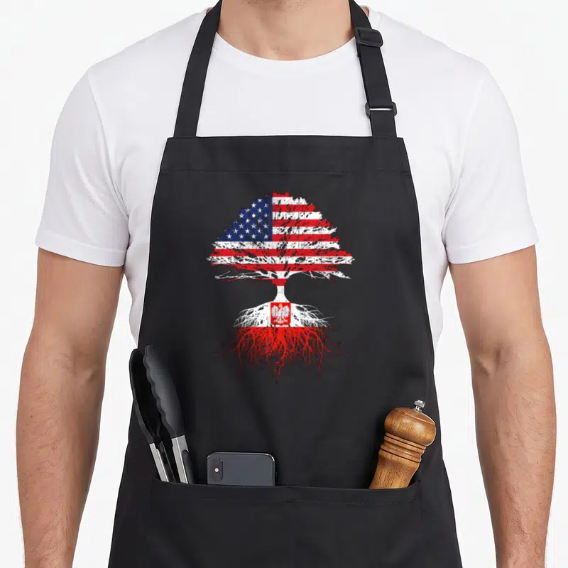 Root grown polish aprons - Distressed tree silhouette filled with USA and Poland flag patterns showing roots and canopy — shown on a black cotton canvas apron against a white background