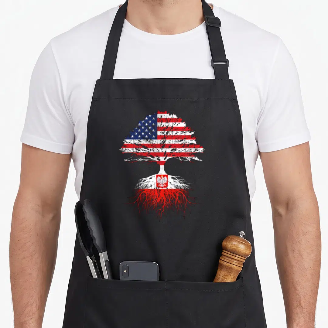 Root grown polish aprons - Distressed tree silhouette filled with USA and Poland flag patterns showing roots and canopy — shown on a black cotton canvas apron against a white background