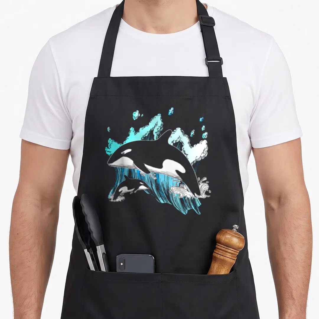 Whale orca dad apron - Line art of adult and baby orca leaping through light blue waves — shown on a black cotton canvas apron against a white background