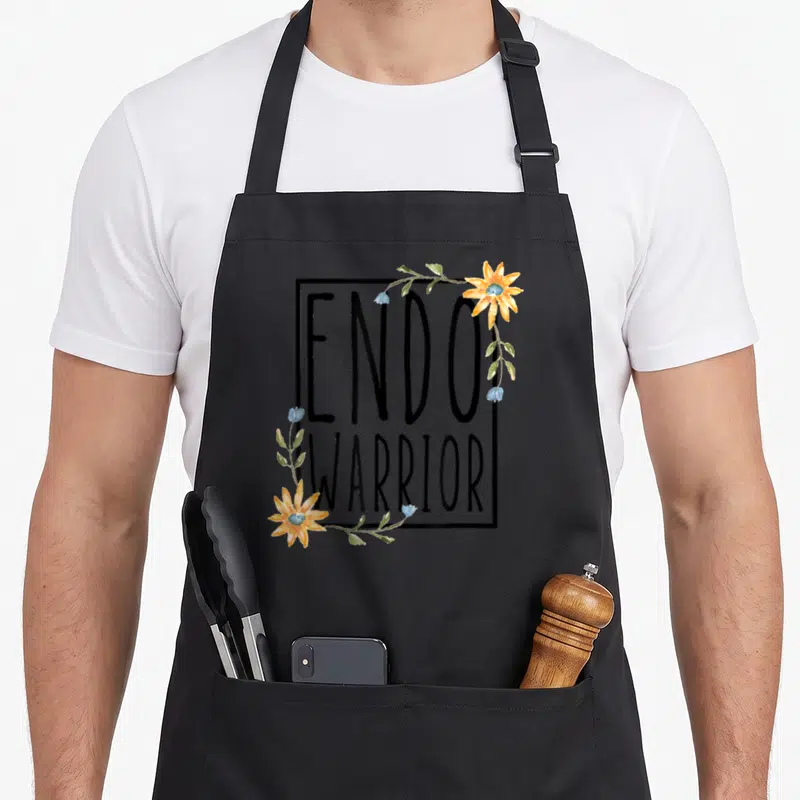 Endo sunflower apron - ENDOWARRIOR text in black frame with yellow sunflowers and blue floral vines — shown on a black cotton canvas apron against a white background