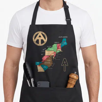 Trail trailer girl apron - Appalachian Trail map with red line, tan logo, and state names including Maine and Georgia — shown on a black cotton canvas apron against a white background