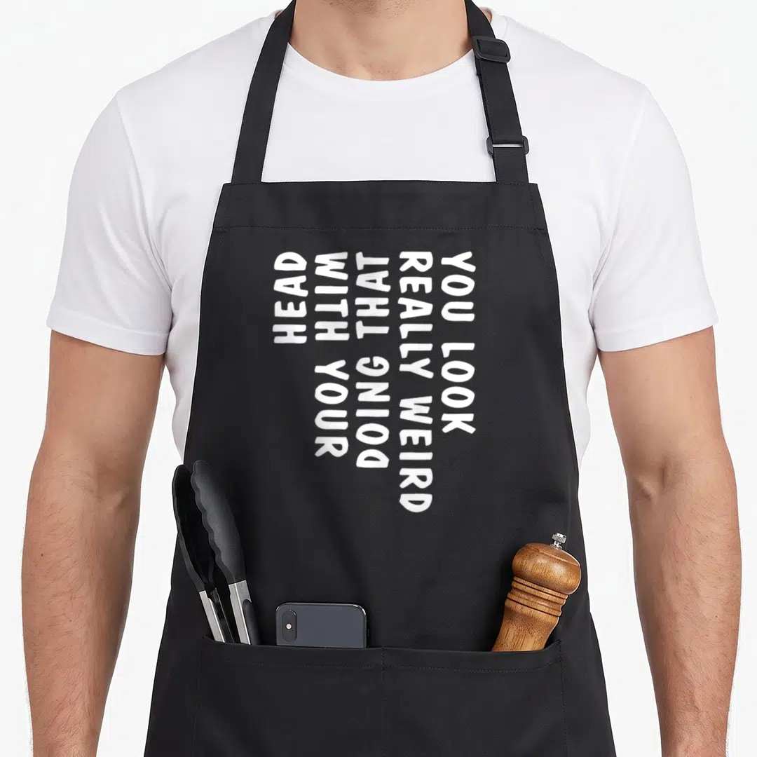 Doing weird aprons - Vertical white text reading You Look Really Weird Doing That With Your Head on dark background — shown on a black cotton canvas apron against a white background