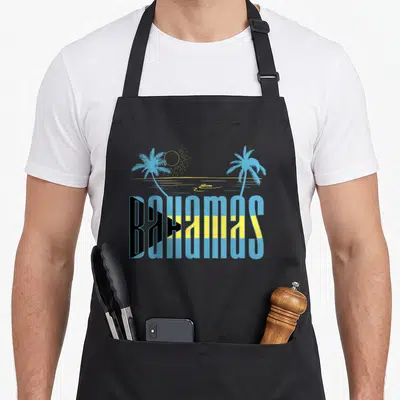 Nassau bahamian apron - BAHAMAS text in flag colors with two palm trees and a sun above an ocean line — shown on a black cotton canvas apron against a white background