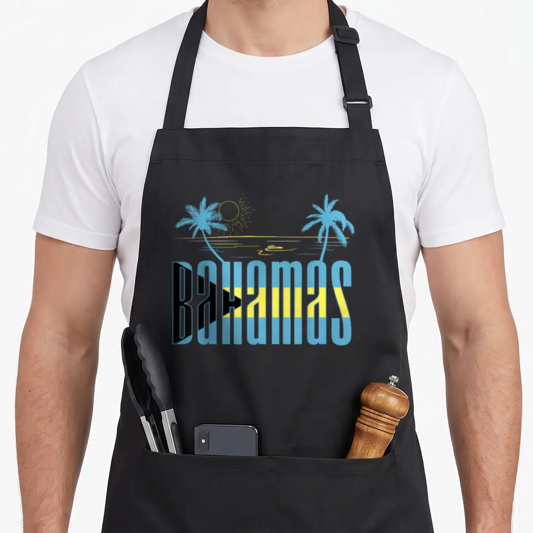 Nassau bahamian apron - BAHAMAS text in flag colors with two palm trees and a sun above an ocean line — shown on a black cotton canvas apron against a white background