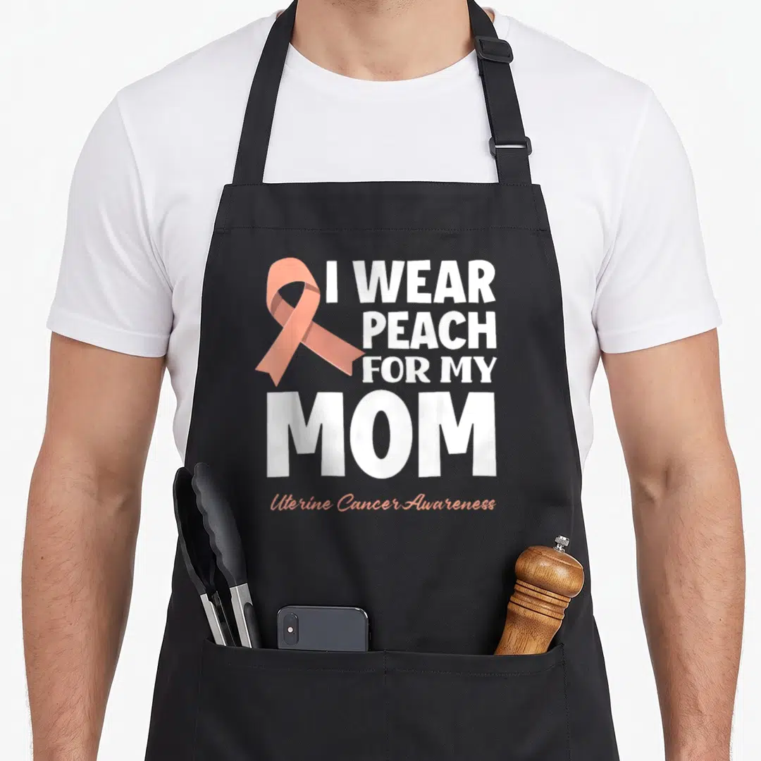 Peach cancer girl apron - I WEAR PEACH FOR MY MOM text with peach ribbon and Uterine Cancer Awareness script — shown on a black cotton canvas apron against a white background