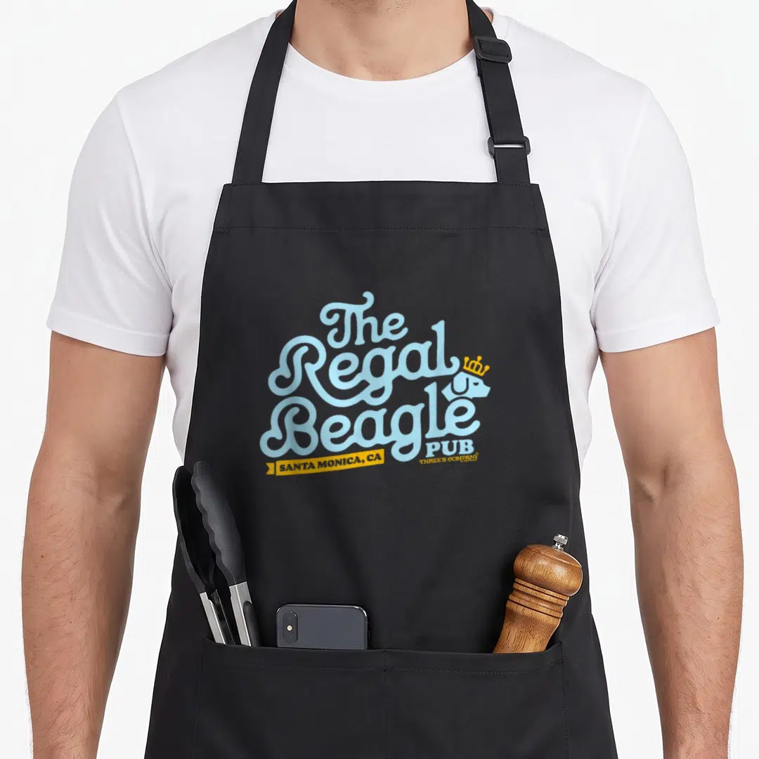 Regal beagle apron - Stacked light blue text The Regal Beagle PUB with white crowned beagle and yellow Santa Monica — shown on a black cotton canvas apron against a white background