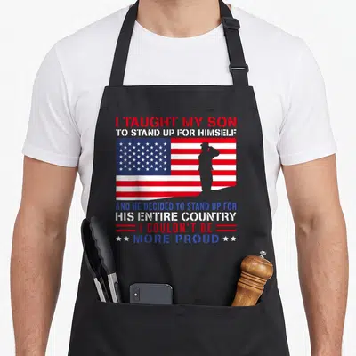 Taught dad and son aprons - USA flag with saluting soldier silhouette and stacked patriotic text in red white and blue — shown on a black cotton canvas apron against a white background