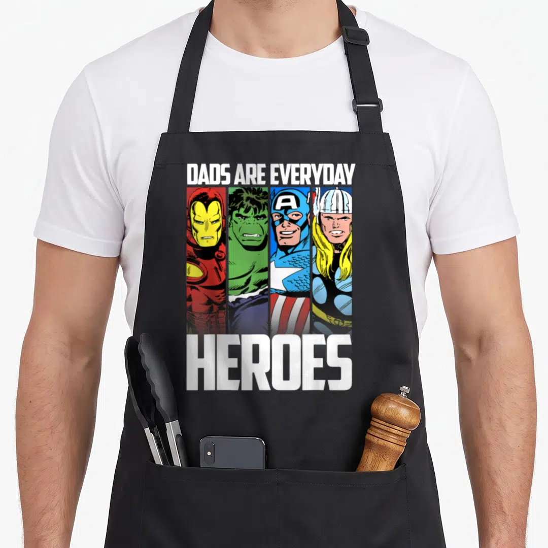 Everyday father day apron - Four vertical superhero panels with Dads Are Everyday Heroes text in red green blue yellow — shown on a black cotton canvas apron against a white background