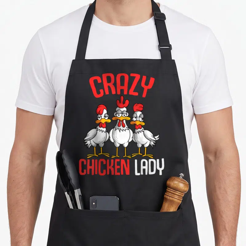 Critter chicken apron - Three cartoon chickens below arched CRAZY text and CHICKEN LADY lettering — shown on a black cotton canvas apron against a white background