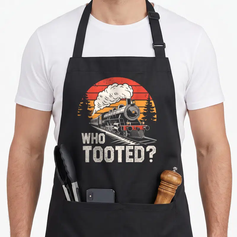 Tooted collector railroad train apron - Retro steam locomotive on tracks with WHO TOOTED text and striped sun background — shown on a black cotton canvas apron against a white background