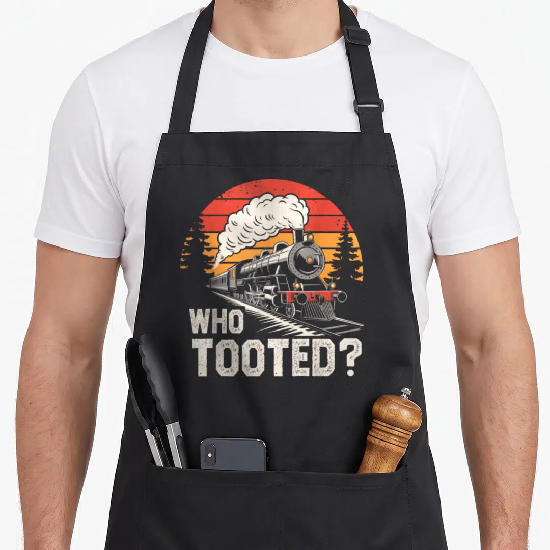Tooted collector railroad train apron - Retro steam locomotive on tracks with WHO TOOTED text and striped sun background — shown on a black cotton canvas apron against a white background