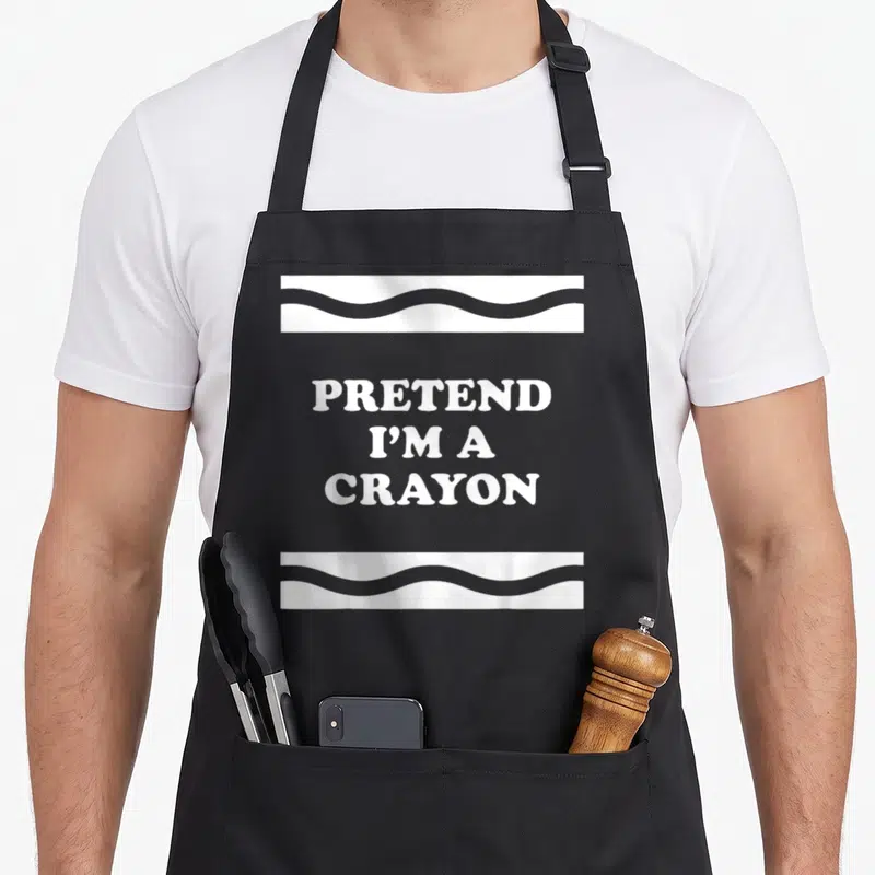 Pretend crayon halloween apron - White text PRETEND I'M A CRAYON between two wavy horizontal bands — shown on a black cotton canvas apron against a white background