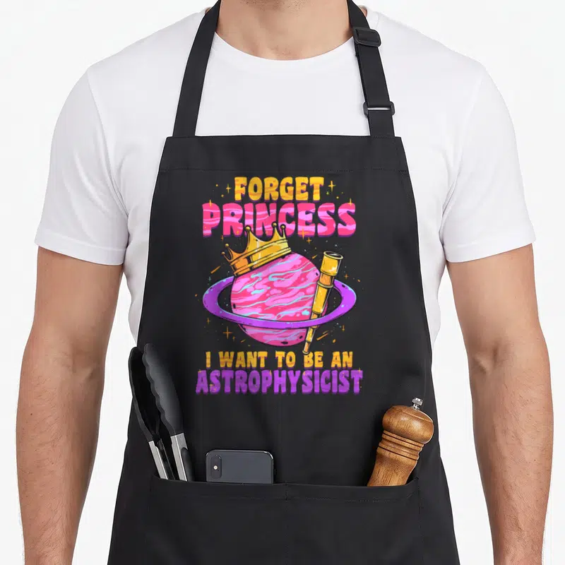 Astrophysicist space princess apron - Pink planet with yellow crown and telescope, stacked text reading Forget Princess — shown on a black cotton canvas apron against a white background