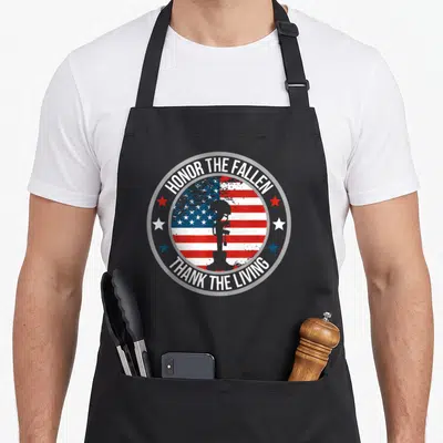 Honor memorial apron - Distressed USA flag circle with helmet rifle boots silhouette and red white blue stars — shown on a black cotton canvas apron against a white background