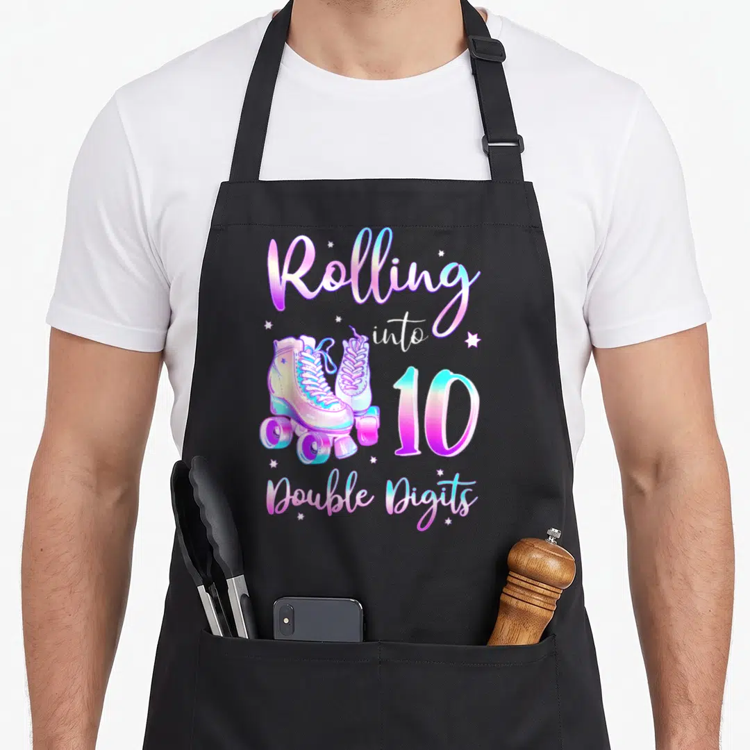 Rolling birthday apron - Rolling into 10 Double Digits text with roller skate illustration and stars — shown on a black cotton canvas apron against a white background