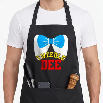 Tweedle couple apron - Cartoon white tooth with blue bow tie and yellow red Tweedle Dee text — shown on a black cotton canvas apron against a white background