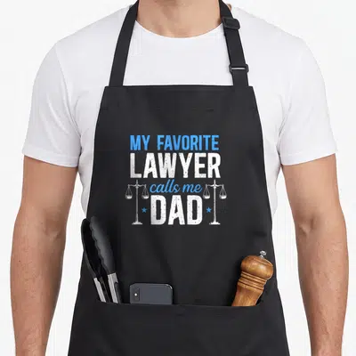 Call lawyer apron - Blue and white text MY FAVORITE LAWYER calls me DAD with two scales of justice and stars — shown on a black cotton canvas apron against a white background