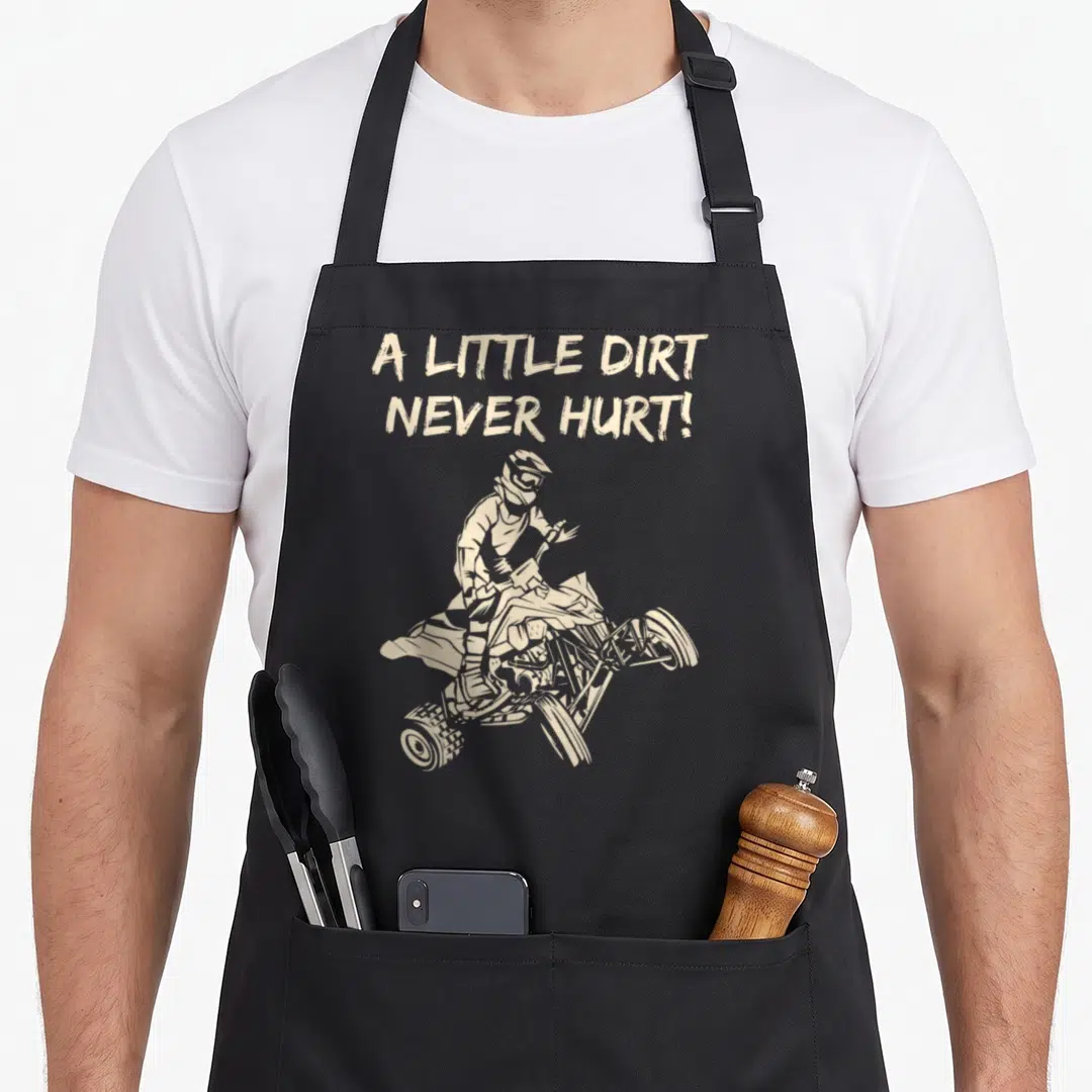 Hurt dirt apron - Beige text A Little Dirt Never Hurt above a jumping ATV rider illustration in distressed style — shown on a black cotton canvas apron against a white background