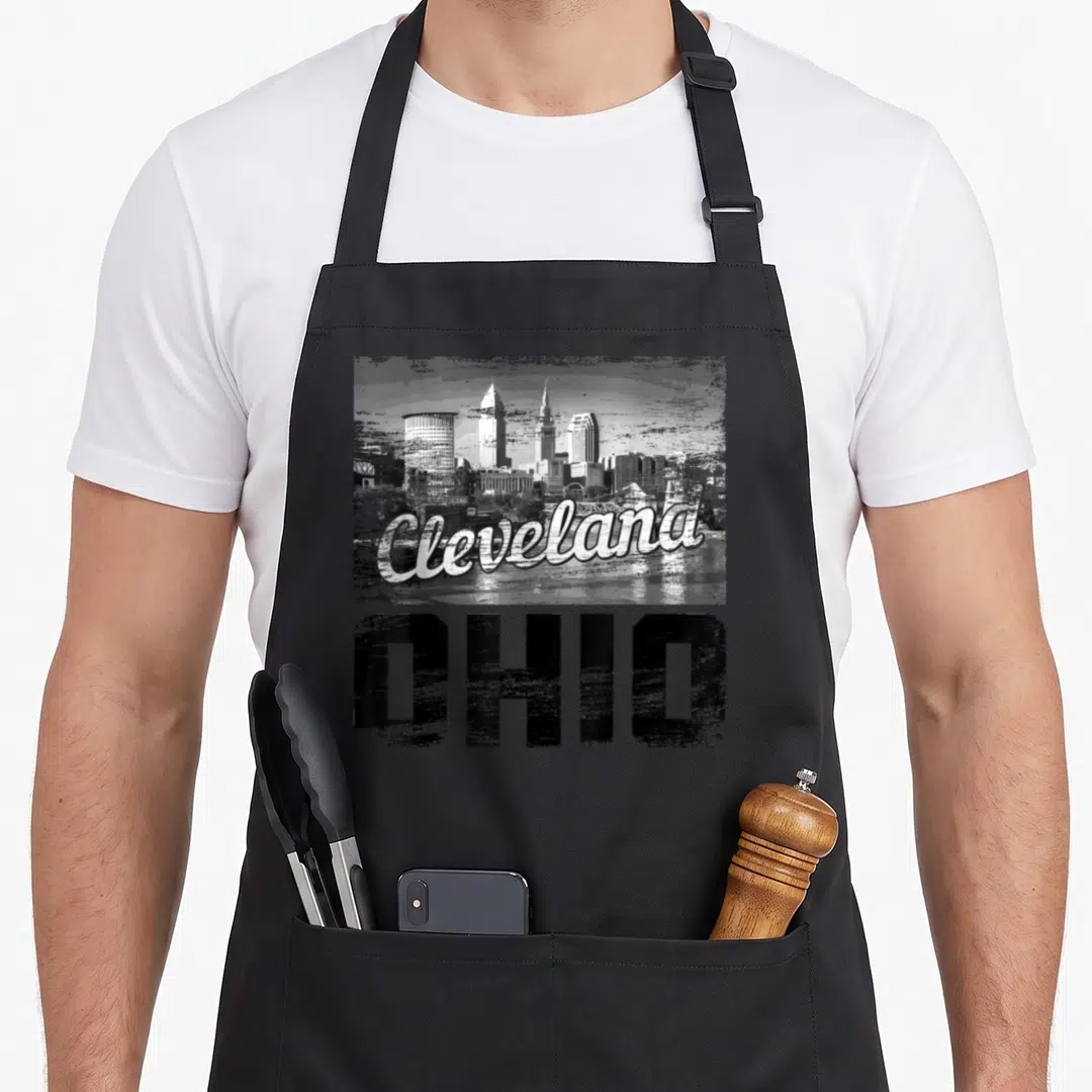 Cleveland ohio skyline pride apron - Grey white black distressed skyline with Cleveland script and OHIO block letters — shown on a black cotton canvas apron against a white background