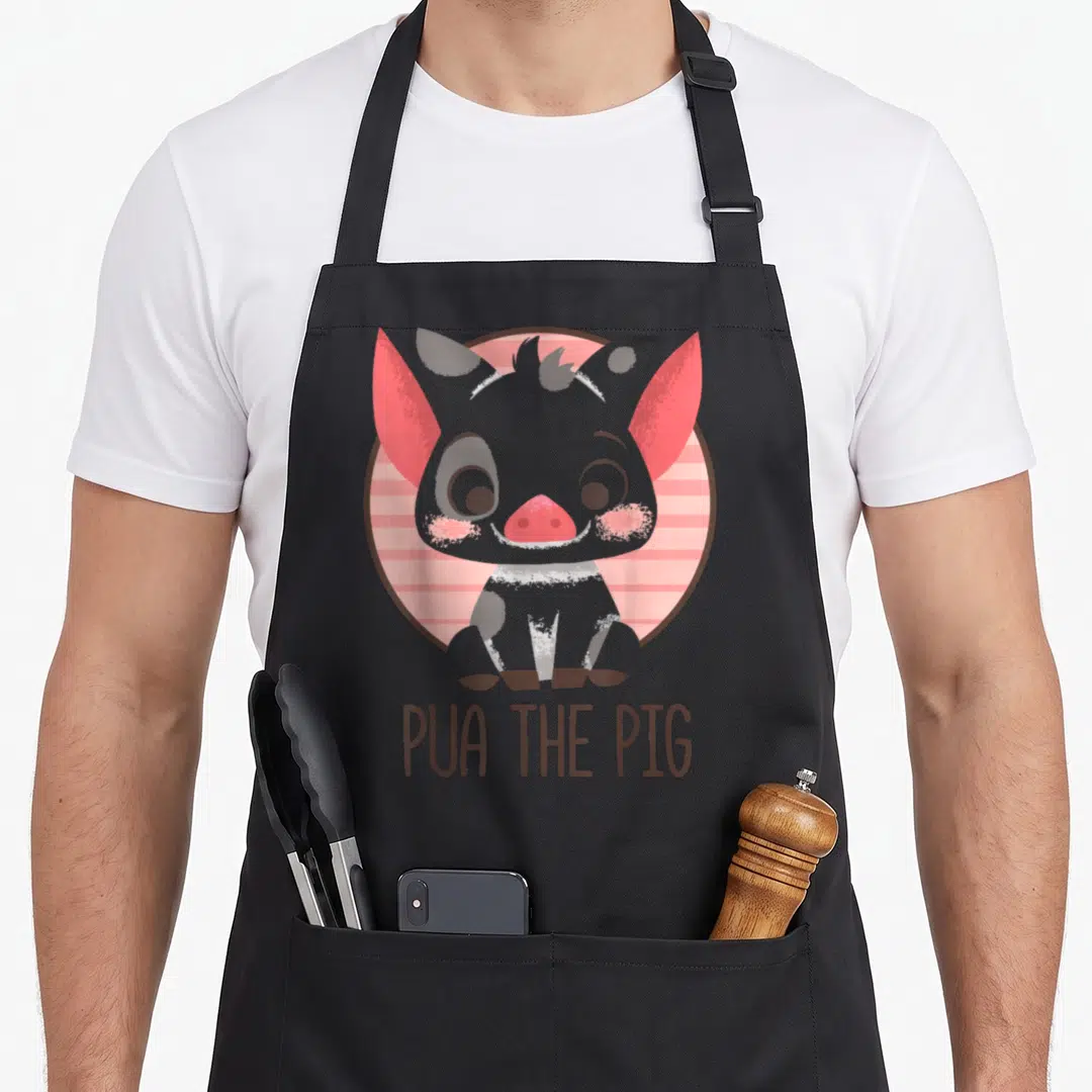 Pua pig apron - Grey cartoon pig sitting on pink striped circle with brown PUA THE PIG text below — shown on a black cotton canvas apron against a white background