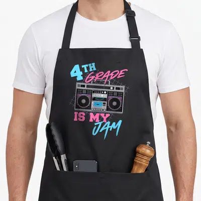 80s teacher apron - Retro boombox illustration with 4th Grade is My Jam text in blue and pink over purple grid — shown on a black cotton canvas apron against a white background