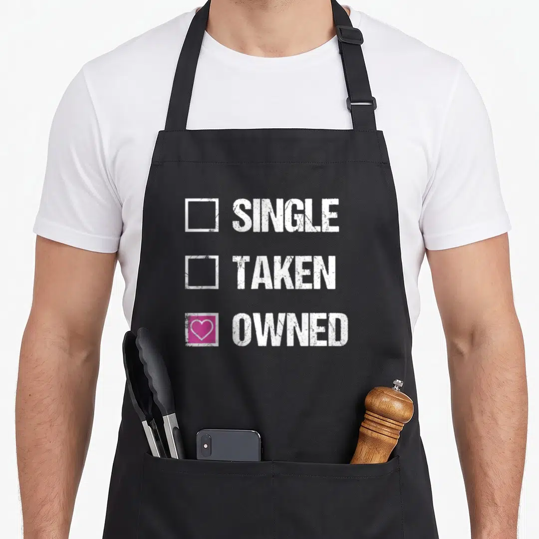Bdsm owner apron - Checklist with SINGLE TAKEN OWNED text and pink box with white heart — shown on a black cotton canvas apron against a white background