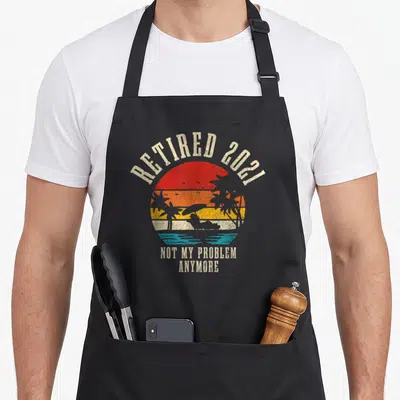 Problem anymore retirement apron - Retro circular sunset with palm trees and text Retired 2021 Not My Problem Anymore — shown on a black cotton canvas apron against a white background
