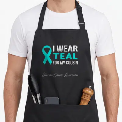 Cousin ovarian cancer awareness apron - Teal ribbon next to white text reading I wear teal for my cousin ovarian cancer — shown on a black cotton canvas apron against a white background