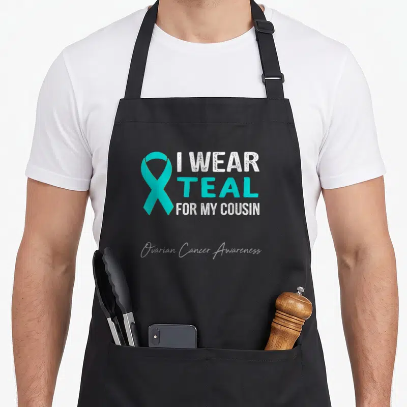 Cousin ovarian cancer awareness apron - Teal ribbon next to white text reading I wear teal for my cousin ovarian cancer — shown on a black cotton canvas apron against a white background